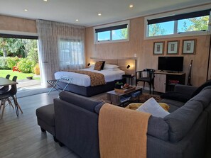 A modern hotel room with a bed, sofa, TV, and a view of the garden.