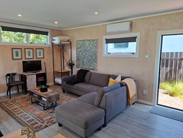 A modern living room with a sofa, ottoman, TV, and a large window.