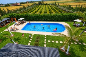 A swimming pool surrounded by a well-maintained lawn, with a view of a distant field and a few buildings.