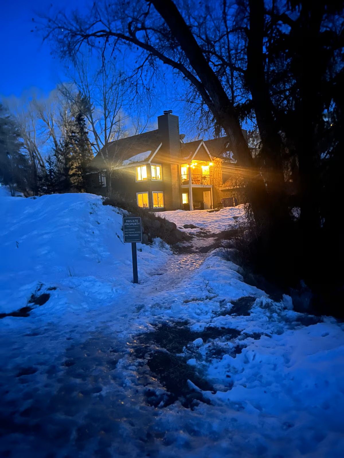 Een twee verdiepingen tellend huis met een verlichte voordeur en ramen, omgeven door een met sneeuw bedekte grond en bomen.