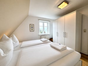 A bedroom with two beds, a window, a radiator, and a wardrobe. - "living in the Countryside", HT 6 (Oldsum)