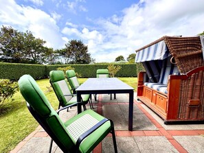 An outdoor patio with a table and chairs, a wicker sofa, and a hedge in the background. - "living in the Countryside", HT 6 (Oldsum)