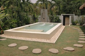 A rectangular pool with a stone border, surrounded by a garden with various plants and a stone pathway leading to a building. - Spacious 3-bedroom house with AC's in every room near all beaches & restaurants (DAUIS)
