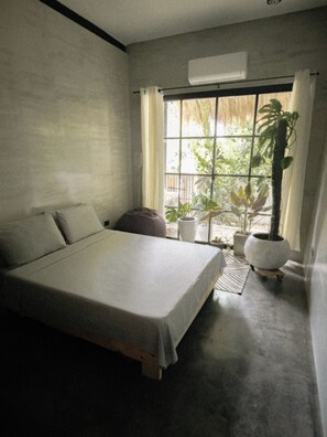 A bedroom with a bed, a window with curtains, a potted plant, and a wall-mounted air conditioner. - Spacious 3-bedroom house with AC's in every room near all beaches & restaurants (DAUIS)