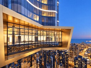 A modern building with a glass facade and a balcony overlooking a cityscape at dusk. - Skyline Suites | Level 54 Sky Getaway, Gym & Pool (Southbank)