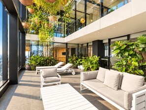 A modern outdoor lounge area with seating and hanging plants. - Skyline Suites | Level 54 Sky Getaway, Gym & Pool (Southbank)