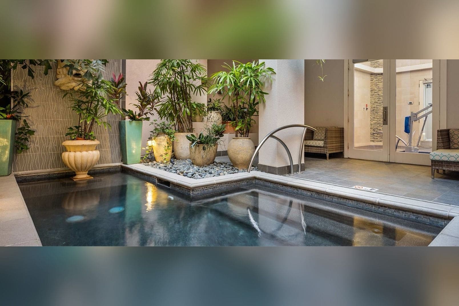 A pool area with a seating area, potted plants, and a stone wall.