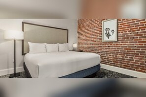 Habitación de hotel con cama, mesita de noche, lámpara, pared de ladrillo y un cuadro enmarcado.