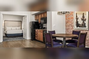 Habitación de hotel compacta con cama, kitchenette y comedor con sillas y mesa.