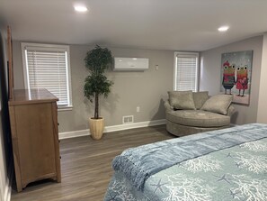 Een slaapkamer met een bed, een houten dressoir, een bloempot, een bank en een wandairconditioner.