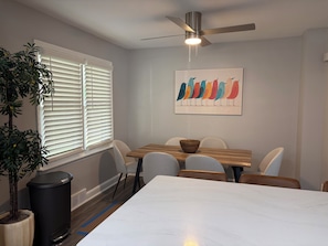 A dining area with a table, chairs, a ceiling fan, a window with blinds, a potted plant, and a trash can. - Deluxe 4 BR 2 BA Neighborhood Gem (Wilmington)