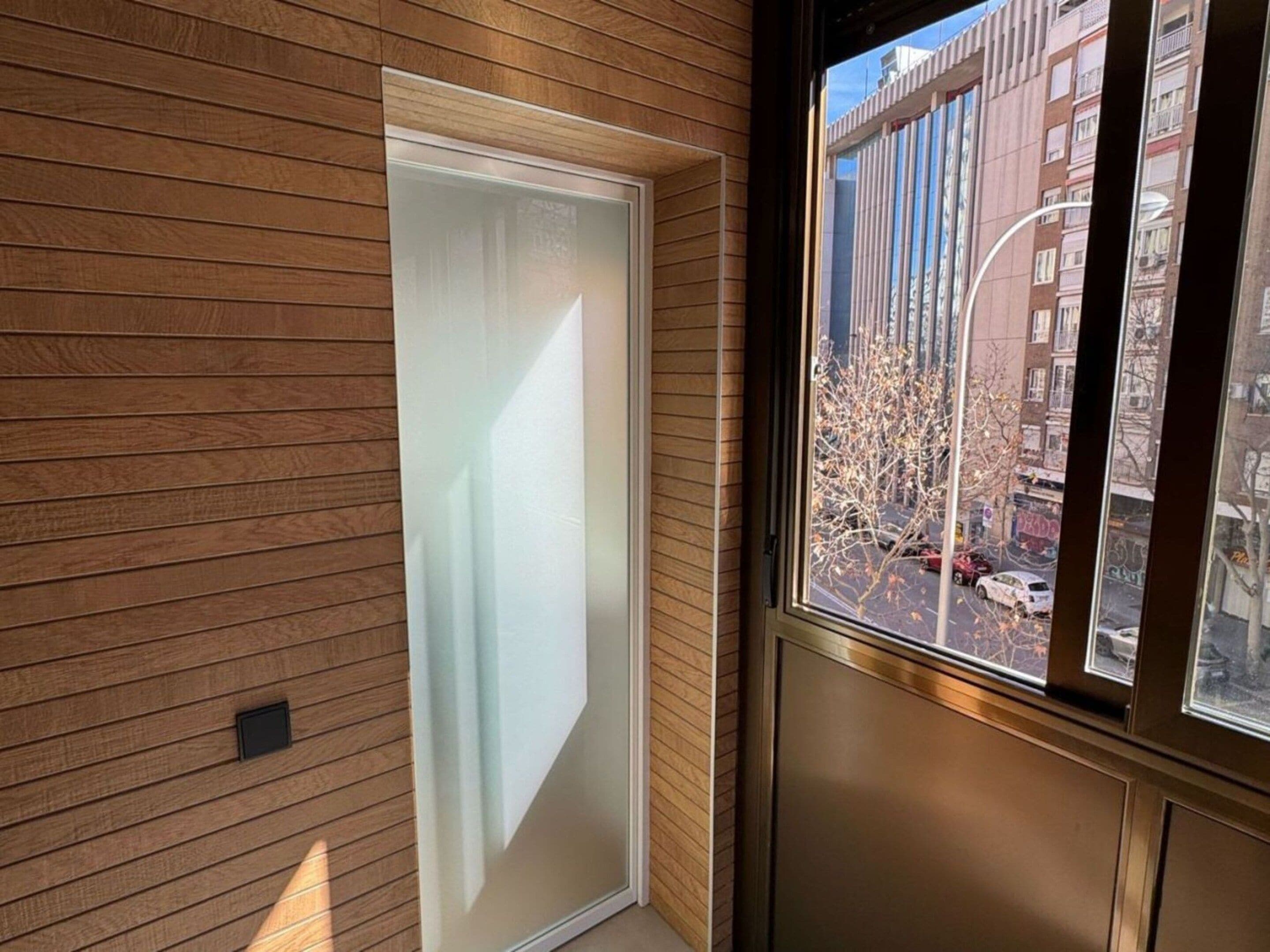 A room with a wooden wall and a window with a view of a cityscape.