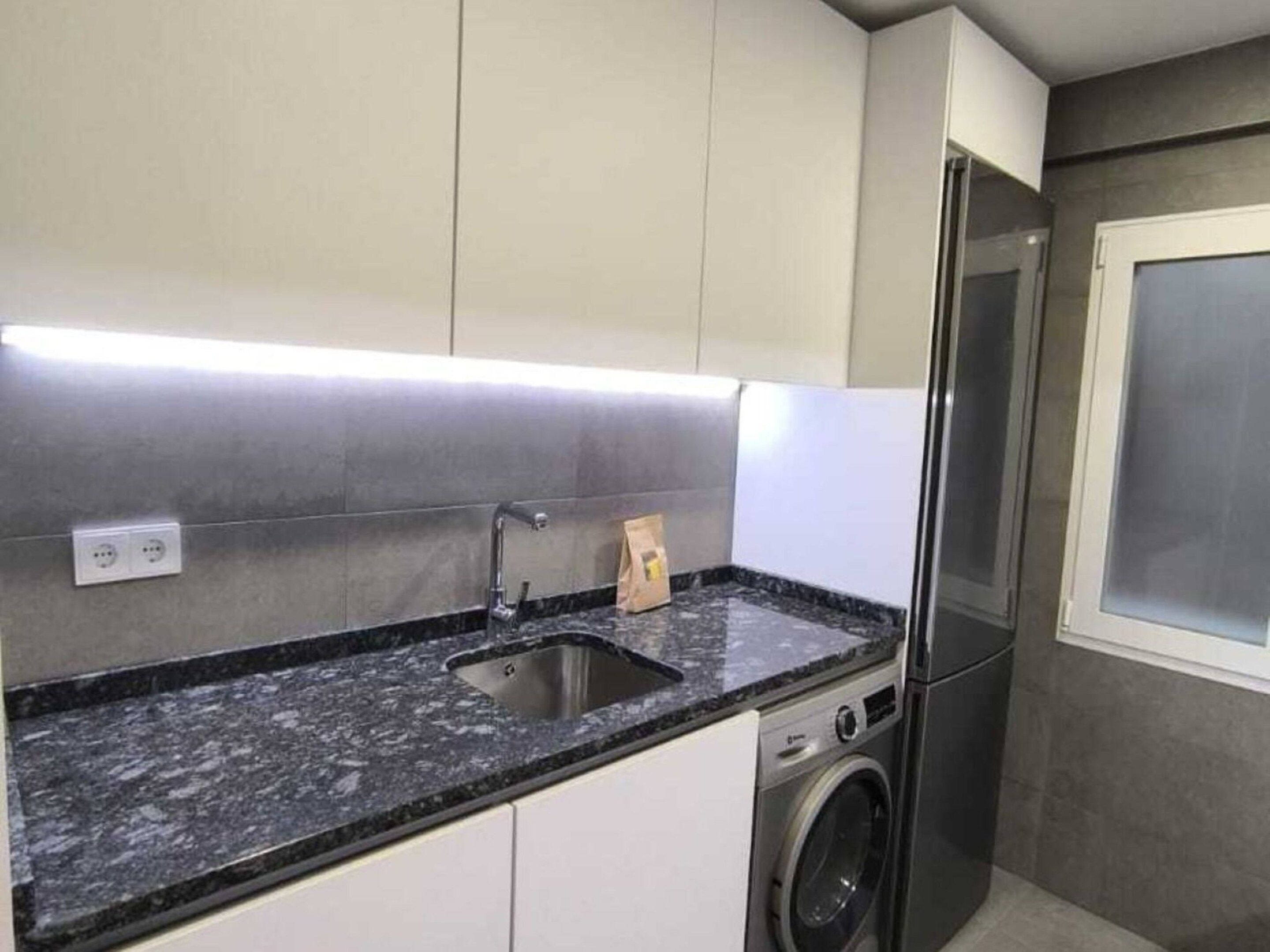 A modern kitchen with a granite countertop, stainless steel sink, and a built-in washing machine.