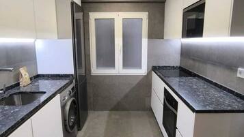 A compact kitchen with a built-in washing machine, a microwave, and a double door window.