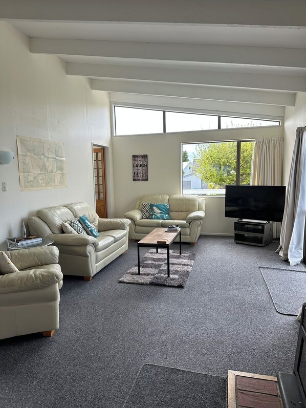 Ein Wohnzimmer mit zwei Sofas, einem Couchtisch, einem Flachbildfernseher und einem großen Fenster mit Vorhängen.