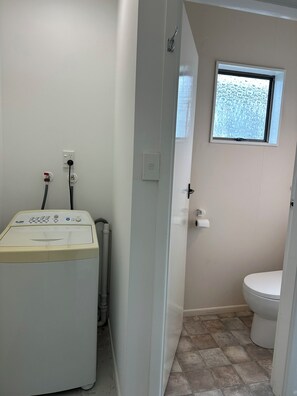 Ein kleines Badezimmer mit einer Waschmaschine, einer Toilette und einem Fenster.