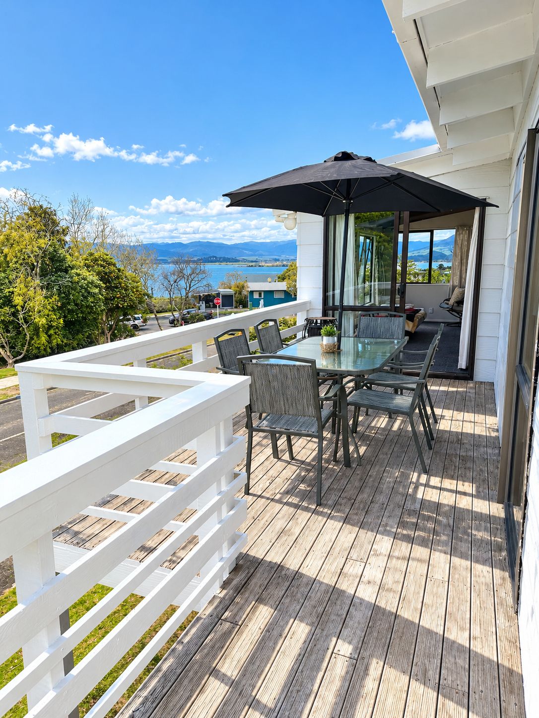 A deck with a glass table and chairs, overlooking a body of water and mountains.