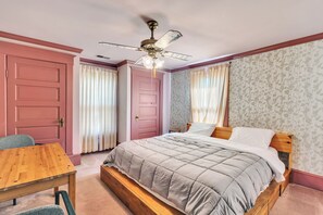 Quarto com cama, mesa de madeira, ventilador de teto e papel de parede estampado.