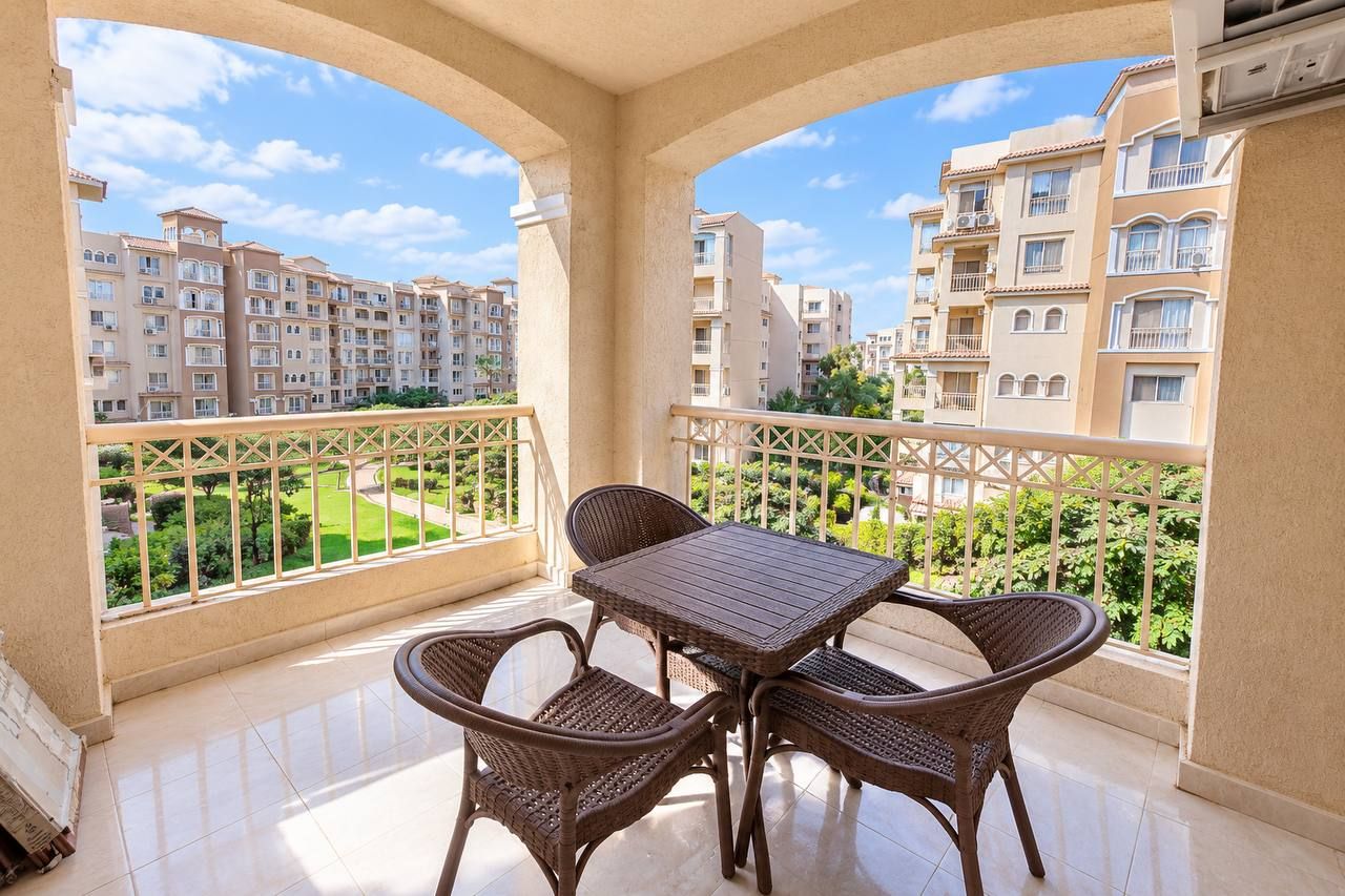 A balcony with a table and chairs, overlooking a residential area with apartment buildings.