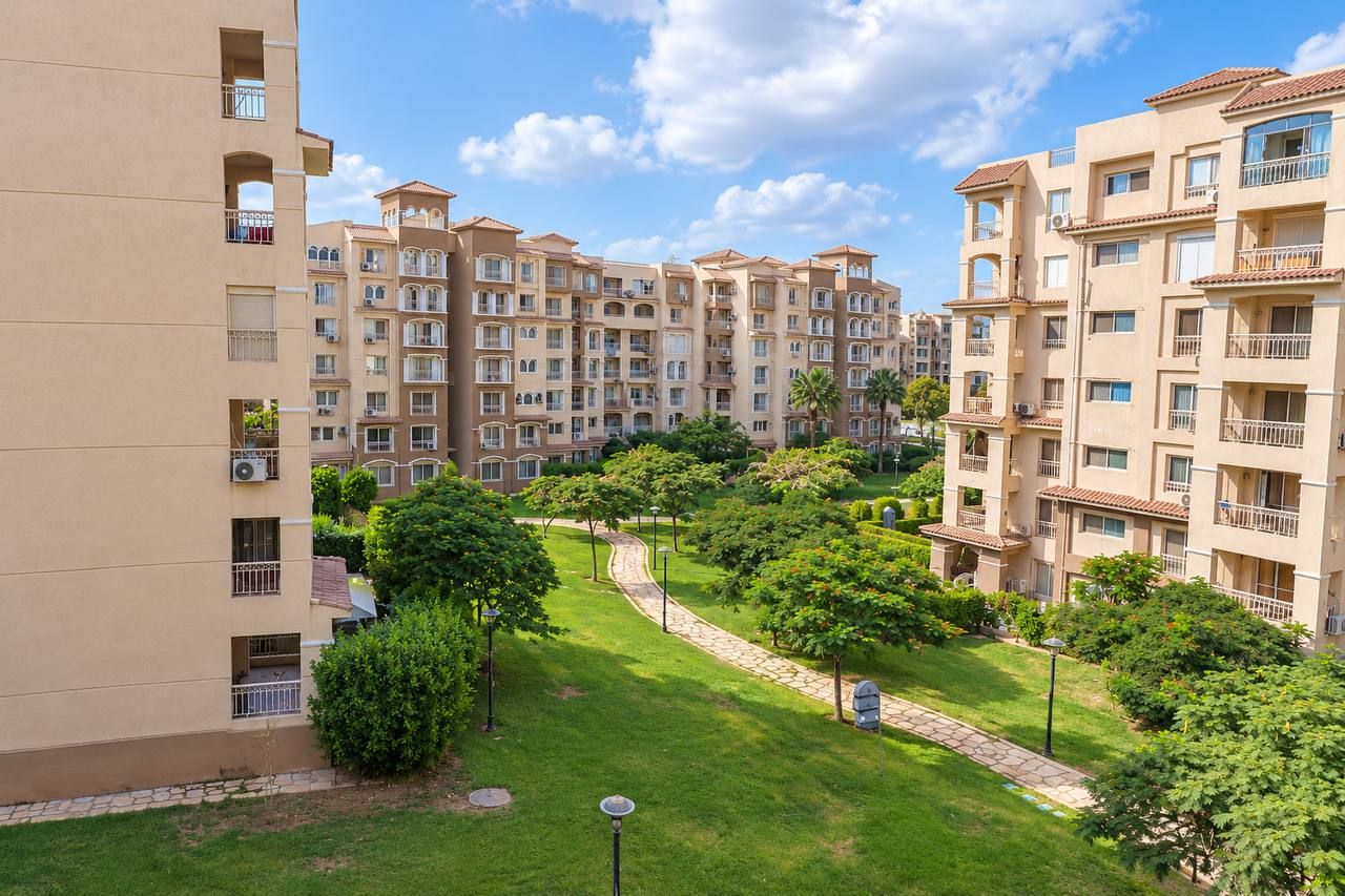 Un immeuble résidentiel à plusieurs étages doté de balcons, d’un jardin aménagé avec un sentier et d’un ciel dégagé.