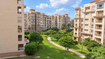Un immeuble résidentiel à plusieurs étages doté de balcons, d’un jardin aménagé avec un sentier et d’un ciel dégagé.