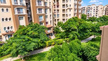 Un immeuble résidentiel à plusieurs étages, doté de balcons, entouré d’une végétation luxuriante et bordé d’un chemin pavé de pierres.