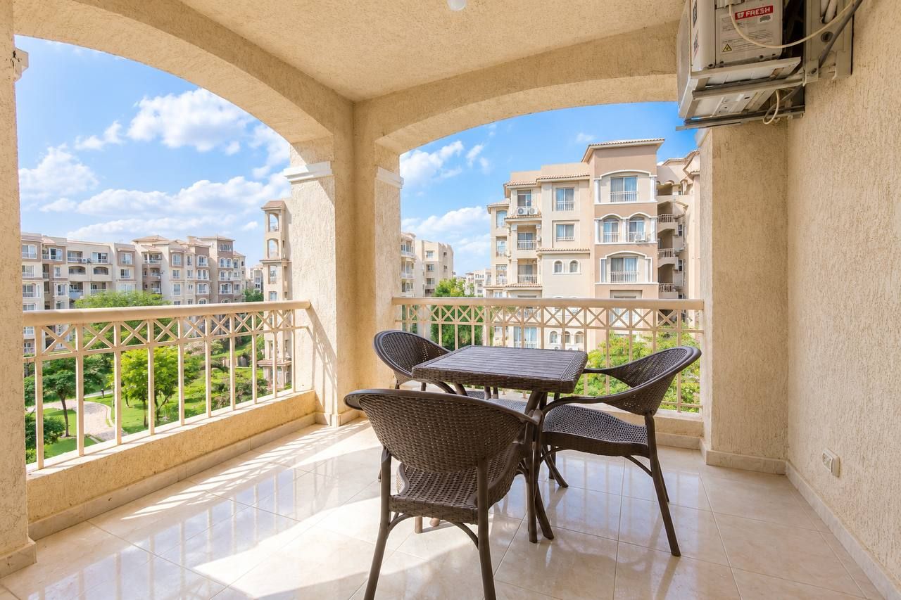 Un balcon avec une table et des chaises, donnant sur un quartier résidentiel composé d’immeubles d’appartements.