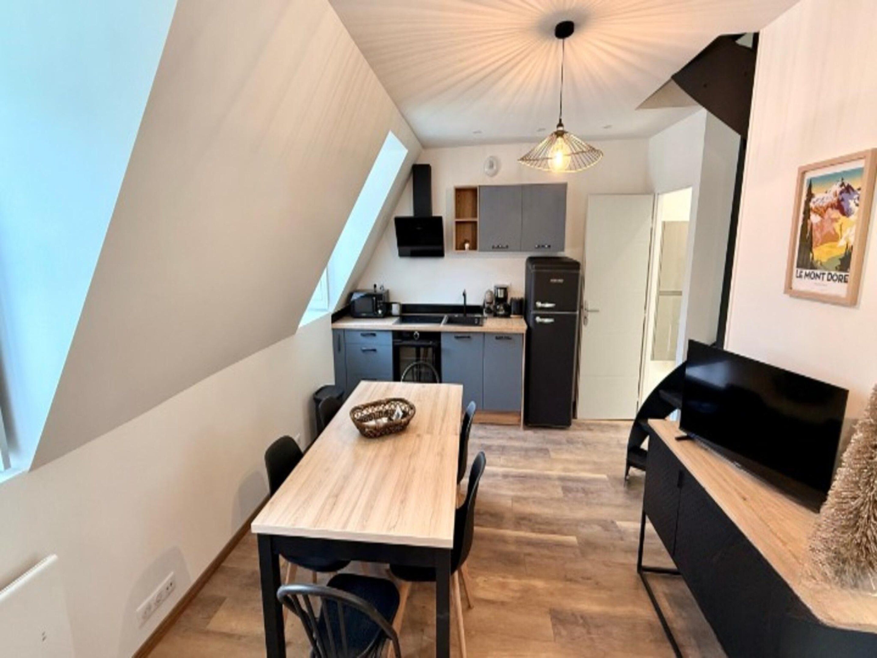 A compact kitchen with modern appliances, a dining area with a wooden table, and a cozy seating area with a sofa.