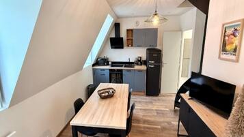 A compact kitchen with modern appliances, a dining area with a wooden table, and a cozy seating area with a sofa.