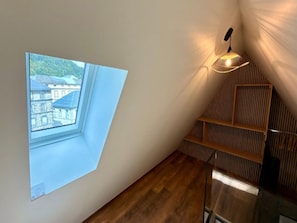 A room with a sloped ceiling, a skylight, a wooden shelving unit, and a hanging light fixture. - Mont-dore Apartment, Mountain View (Mont-Dore)