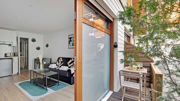 A modern apartment with a sliding glass door leading to a balcony, a kitchen area, and a living space with a sofa and coffee table.