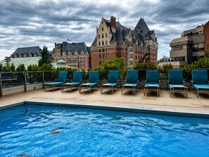 Una piscina con sillas de descanso, un edificio histórico grande al fondo y un cielo nublado.