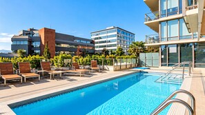 Una piscina sul tetto con lettini, circondata da edifici moderni e vegetazione.