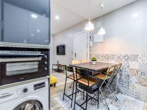 A compact kitchen with a built-in oven, a washing machine, and a dining area with a table and chairs. - Apartment Near Retiro Park (Madrid)