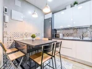 A modern kitchen with white cabinets, a tiled backsplash, and a dining area with a table and chairs. - Apartment Near Retiro Park (Madrid)