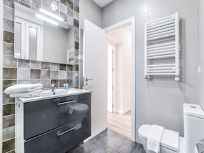 A modern bathroom with a grey tiled wall, a white sink, a black cabinet, and a white toilet. - Apartment Near Retiro Park (Madrid)