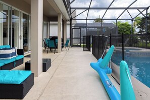 Ein überdachter Außenbereich mit Pool, Liegestühlen und Grill.