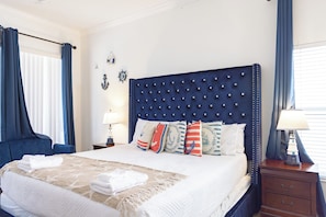 A hotel room with a large bed, blue curtains, nautical-themed decor, and a nightstand with a lamp. - 7BR Villa Near Disney / FREE Pool Heat, Hot Tub, Game Room / Sleeps 14 (Clermont)