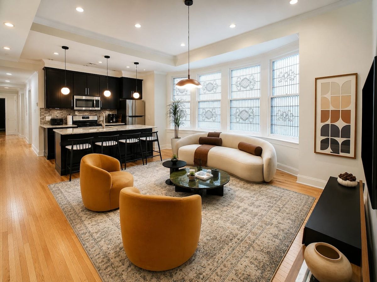 A modern living room with a sofa, two armchairs, a coffee table, and a dining area with a kitchen in the background.