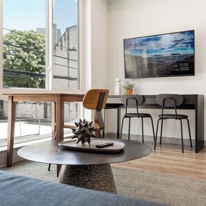 A modern living room with a round table, two chairs, a sofa, a TV mounted on the wall, and a window with a view of the outside. - Stylish 1BD near UPenn & Drexel | Queen Bed (Philadelphia)