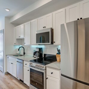 A modern kitchen with white cabinetry, stainless steel appliances, a microwave, and a coffee maker. - Stylish 1BD near UPenn & Drexel | Queen Bed (Philadelphia)
