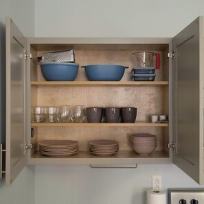 A kitchen cabinet with shelves containing bowls, glasses, and plates. - Business Center City Studio | By Rafa Properties (Philadelphia)
