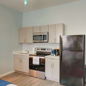 A compact kitchen with a stainless steel refrigerator, a microwave, an oven, and a sink. - Business Center City Studio | By Rafa Properties (Philadelphia)