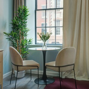 A room with a round table, two chairs, a potted plant, and a window with curtains. - Business Center City Studio | By Rafa Properties (Philadelphia)