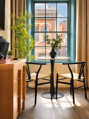 A room with a table and chairs, a window with a view of buildings, and a plant on the table. - Charming Center City Studio | By Rafa Properties (Philadelphia)