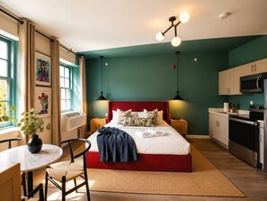 A modern bedroom with a red bed, a dining area with a round table, and a kitchenette with a microwave. - Charming Center City Studio | By Rafa Properties (Philadelphia)