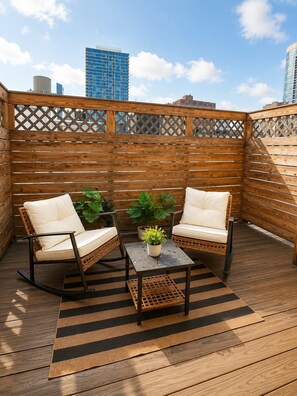 A wooden deck with two wicker chairs and a table, surrounded by a lattice fence. - Chic 1BD in RittenHouse Sq | Balcony (Philadelphia)