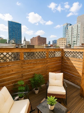 A rooftop patio with wooden decking, a cushioned chair, a small table, and potted plants. - Chic 1BD in RittenHouse Sq | Balcony (Philadelphia)