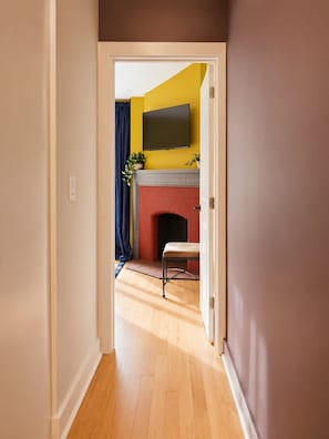 A hallway leading to a room with a fireplace, a television mounted above it, and a door with a light switch. - Chic 1BD in RittenHouse Sq | Balcony (Philadelphia)