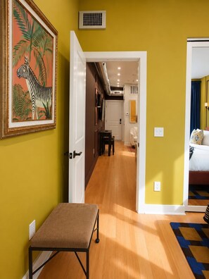 A hallway with a bench, a zebra painting, and a door leading to a bedroom with a bed and a patterned rug. - Chic 1BD in RittenHouse Sq | Balcony (Philadelphia)